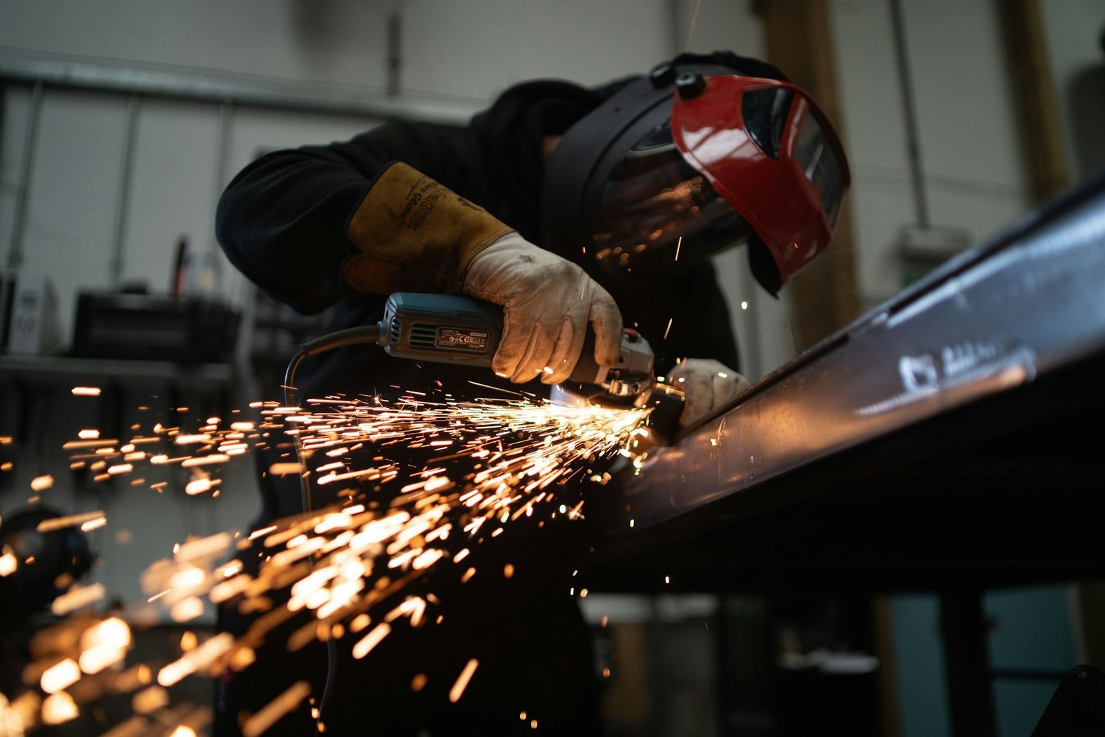 Fabricator grinding a steel beam with sparks flying in a UK fabrication workshop